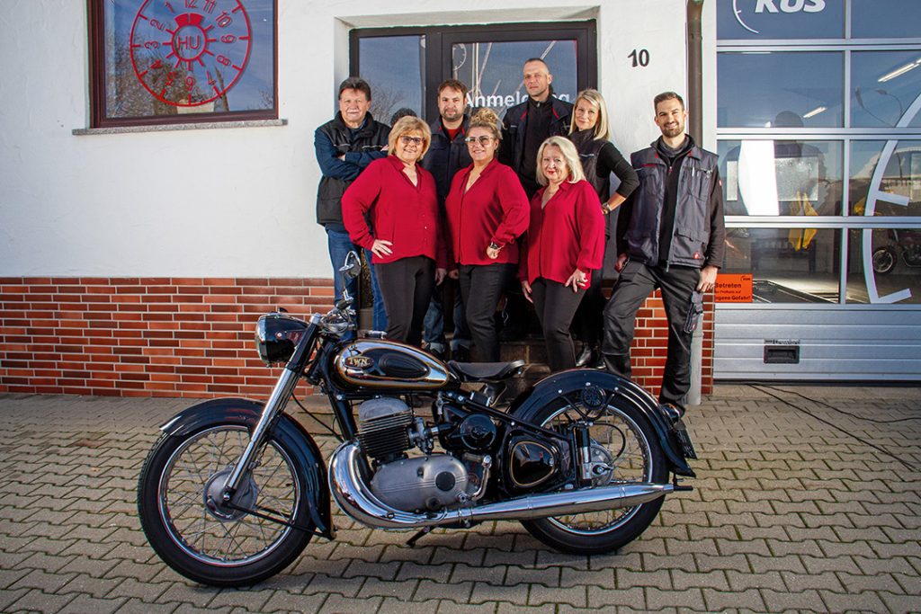 Das Bild zeigt das Team des Ing.-Büro Prüfcenter Ebert vor dem Eingang zum Prüfcenter in Langenzenn. Weiterhin ist im Vordergrund ist ein Motorrad erkennbar.