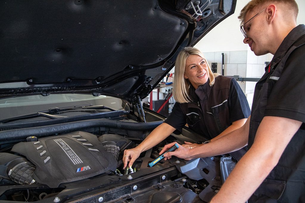 Das Bild zeigt den Blick in den geöffneten Motorraum eines SUV, den zwei Mitarbeiter des Ing-Büro Prüfcenter Ebert genauer inspizieren.