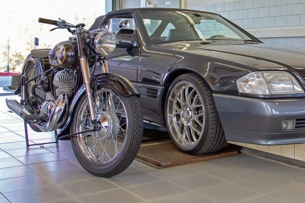Das Bild zeigt zwei historische Fahrzeuge, die als Oldtimer gelten: ein Motorrad und einen PKW in der Prüfhalle.